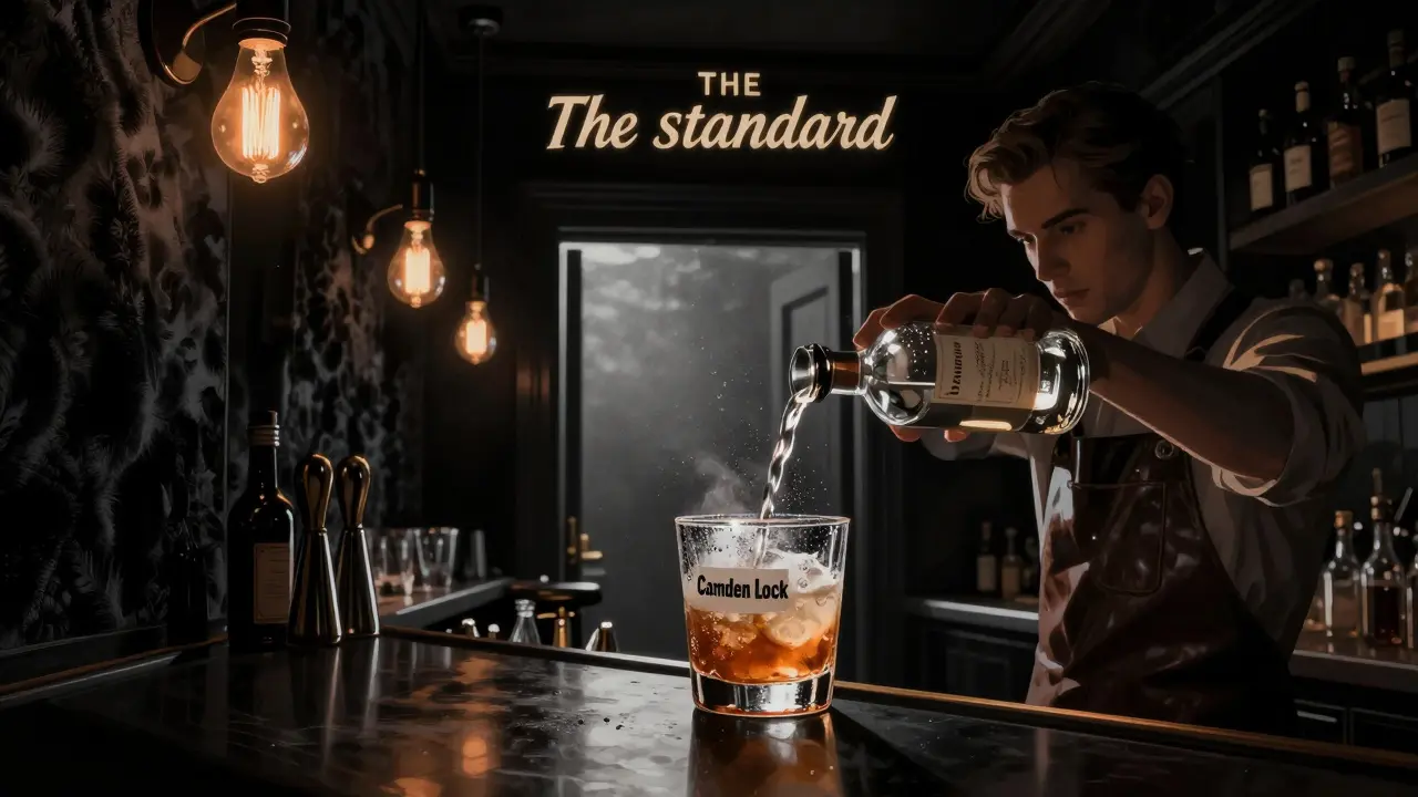 Dark, moody bar with Edison bulbs and velvet walls, glass of mezcal cocktail in focus.